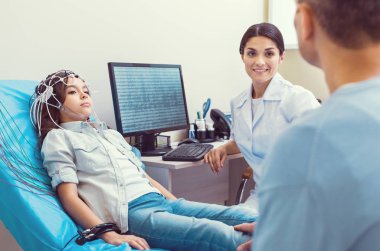 Scared little girl undergoing electroencephalography procedure at lab clipart