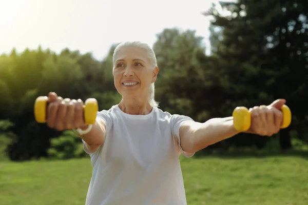 Örömteli idős hölgy sugárzó rövid idő emelés a súlyzók — Stock Fotó