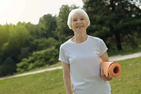 Alegre aposentado senhora posando com fitness mat ao ar livre — Fotografia de Stock