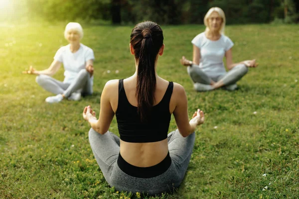 Anziani che praticano yoga con giovani allenatrici — Foto Stock