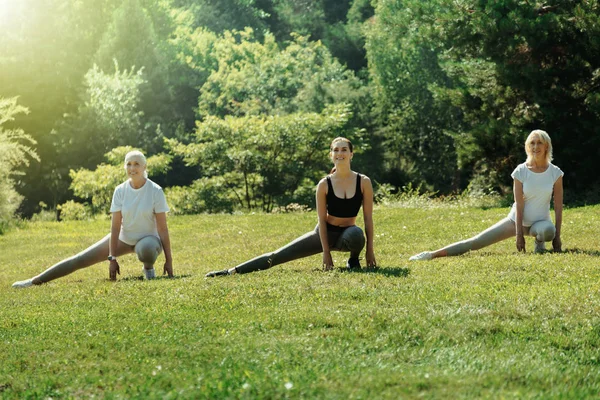 Mujeres mayores activas y entrenadoras jóvenes estirando sus piernas — Foto de Stock