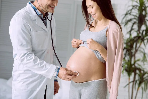 Médico agradável alegre usando um estetoscópio — Fotografia de Stock