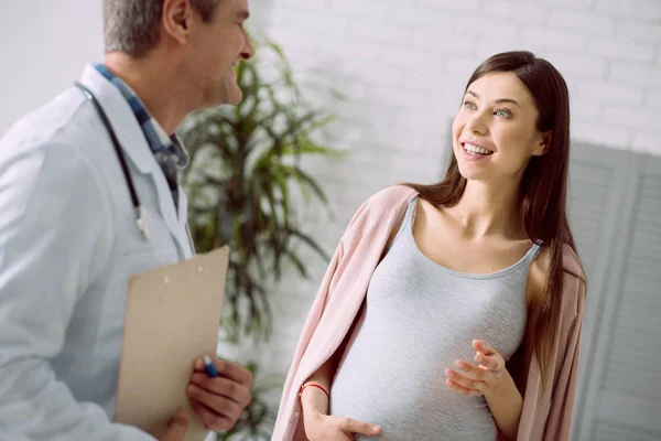 我的幸福 开朗美丽的孕妇抚摸她的腹部和微笑 而她的医生说话 — 图库照片