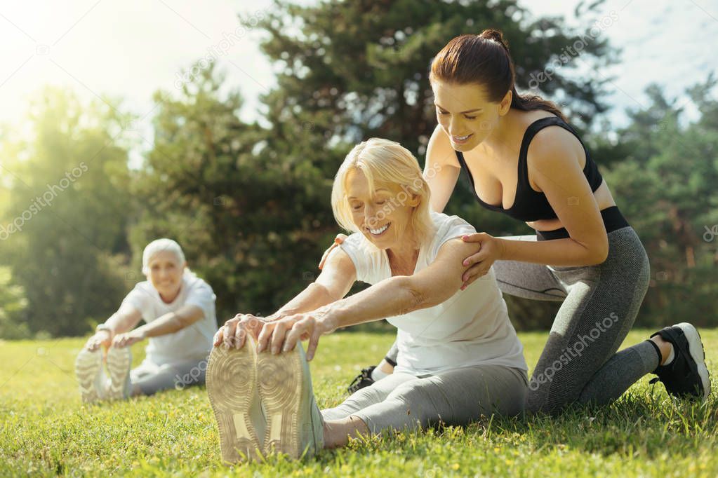 Mindful young lady helping retired woman with exercise