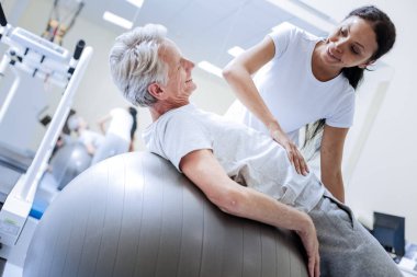 Engelli erkek incelenirken gülümseyen neşeli deneyimli doktor