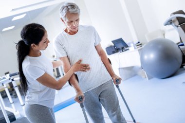 Yaşlı adam onun koltuk değneği üzerinde yürümeye çalışırken eğilerek konsantre