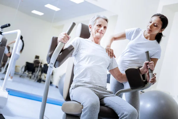 Entusiástico baby boomer usando máquina de peso em um centro de reabilitação — Fotografia de Stock