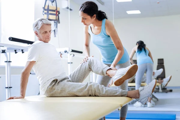 Calm doctor bending the knee of her patient and looking at him — Stock Photo, Image