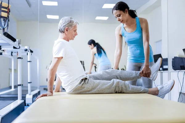 Freundliche professionelle Trainerin wärmt die verletzten Muskeln ihrer betagten Patientin — Stockfoto