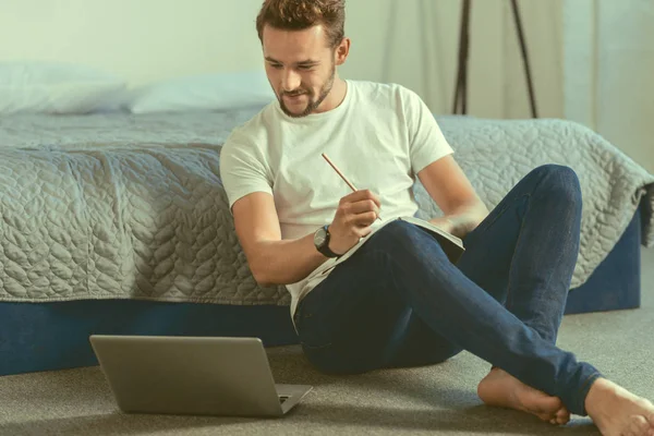 Усміхнений студент чоловічої статі, що працює над домашнім завданням на ноутбуці — стокове фото