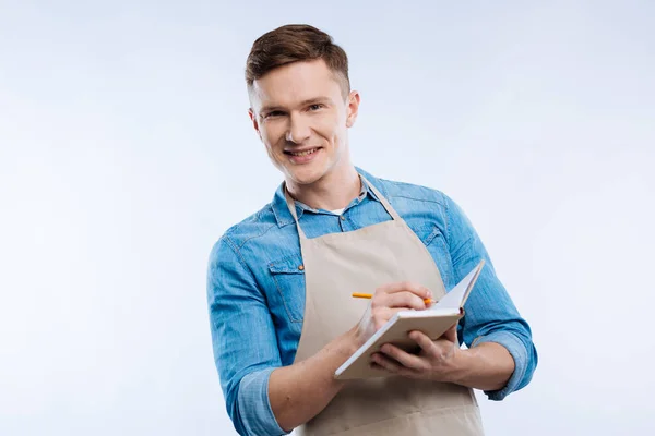 Positiver freudiger Mann, der in sein Notizbuch schreibt — Stockfoto