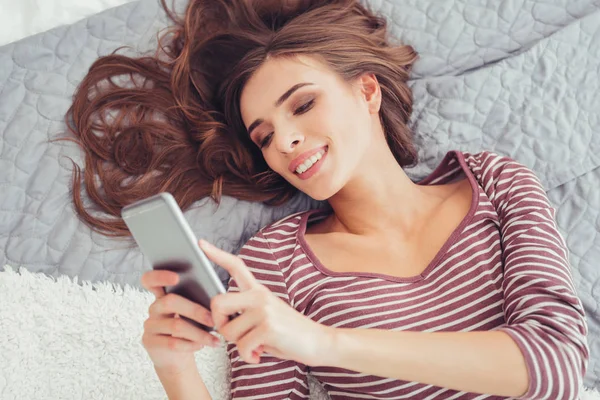 Primer plano de chica encantadora usando el teléfono móvil en la cama — Foto de Stock