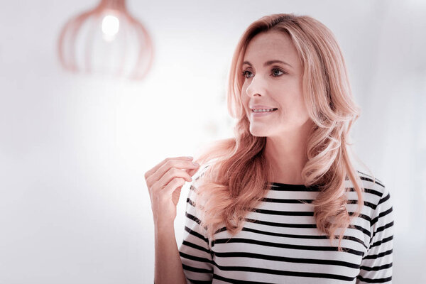 Красивая женщина смотрит вдаль, прикасаясь к волосам и улыбаясь
