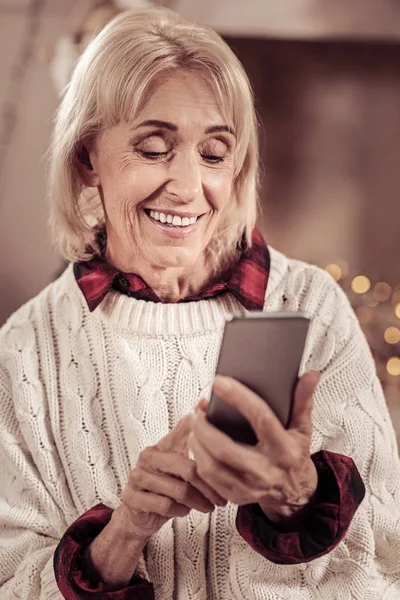 Zainteresowana kobieta uśmiechający się stały i za pomocą jej telefon. — Zdjęcie stockowe