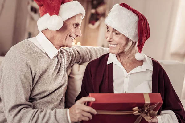 Encantador casal sênior sorrindo e segurando um presente . — Fotografia de Stock