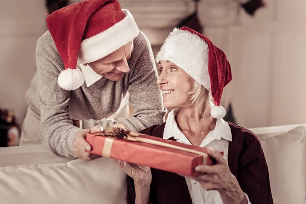 Mujer linda satisfecha sosteniendo un regalo mirando a su marido . — Foto de Stock