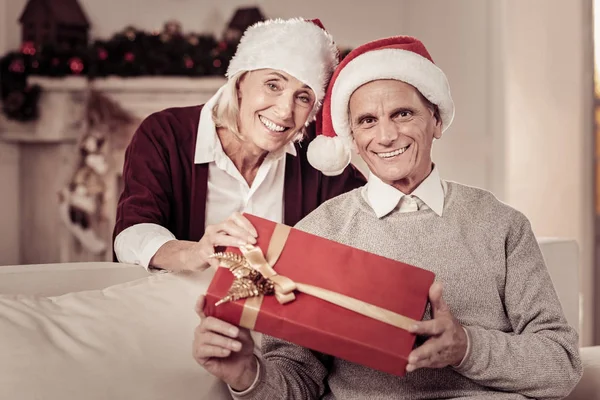 Agradable pareja mayor sonriendo y sosteniendo un regalo . — Foto de Stock