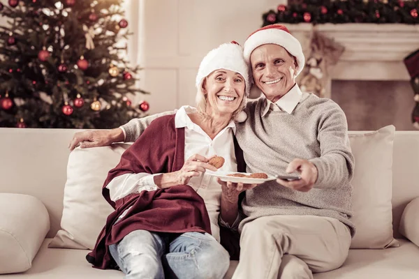 Happy pleasant couple sitting on the sofa and looking straight. — Stock Photo, Image