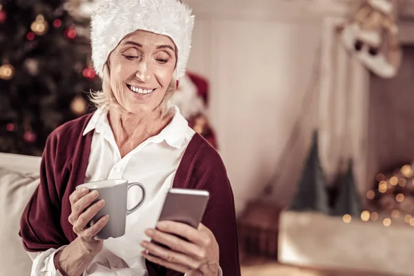 Agréable femme intéressée souriant et utilisant le téléphone portable . — Photo