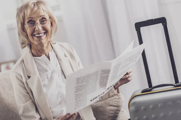 Strahlende Frau liest Artikel in der Nähe ihres Gepäcks — Stockfoto