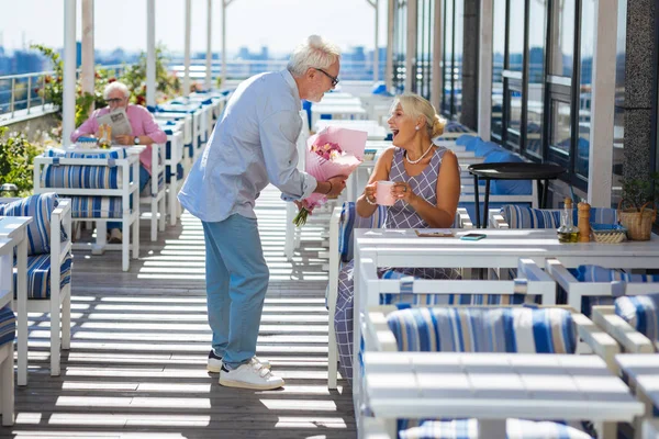 Положительный хороший пожилой мужчина дарит цветы своей жене — стоковое фото