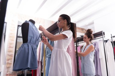 Moda tarafında. Düşük açılı metre kullanırken tulum üzerinde çalışan profesyonel kadın terzi