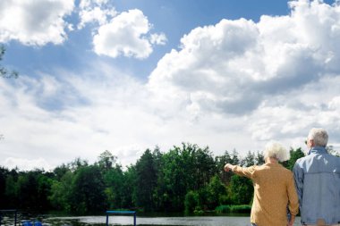 Kocasıyla ayakta ve ağaçlara doğru işaret eden kadın kıdemli