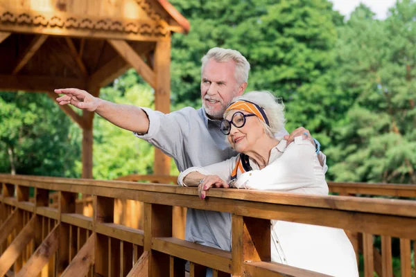 Pensionista confiante abraçando sua esposa e apontando para a distância — Fotografia de Stock