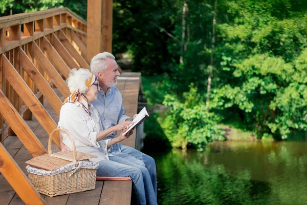 Pensionista activo haciendo picnic en el puente y sosteniendo el cuaderno — Foto de Stock