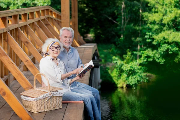 Adorables personas mayores sonriendo mientras están sentadas con un cuaderno brillante — Foto de Stock