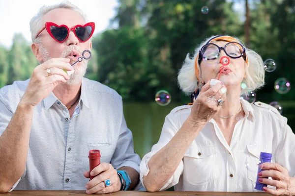 Vicces nyugdíjasok napszemüveget visel, és fúj a szappanbuborékok — Stock Fotó