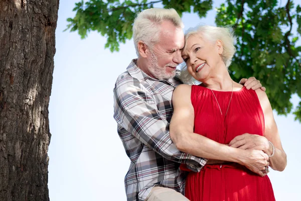 Hermosa pareja de ancianos de pie bajo el árbol y abrazándose — Foto de Stock