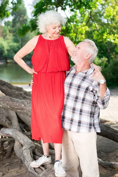 Счастливая старшая женщина стоит на бревне и смотрит на своего мужа — стоковое фото