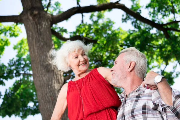 Amable pensionista mirando a su esposa de pie y sonriéndole — Foto de Stock