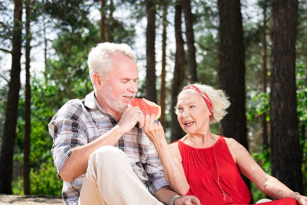 Kind senior woman looking at her husband while giving his watermelon