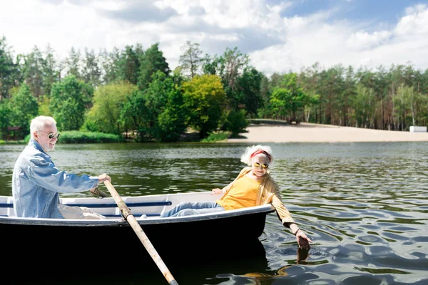 Старший гребёт на лодке, пока его любопытная жена касается воды. — стоковое фото