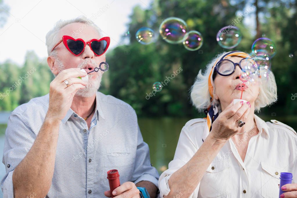 Positive senior couple feeling good while blowing soap bubbles