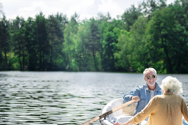 Atraente pensionista remando o barco e sorrindo alegremente para sua esposa — Fotografia de Stock
