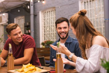 Üç genç arkadaş barda oturmuş ve sohbet ederken gülüyor