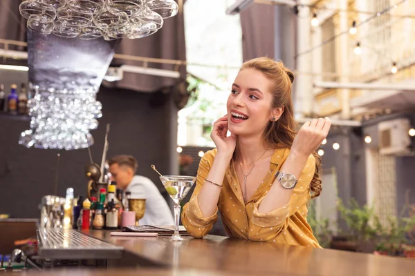 Chica joven expresiva sentada en el mostrador del bar y mirando feliz — Foto de Stock