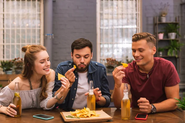 Amigos hambrientos sentados en el bar y comiendo sabrosas patatas fritas —  Fotos de Stock