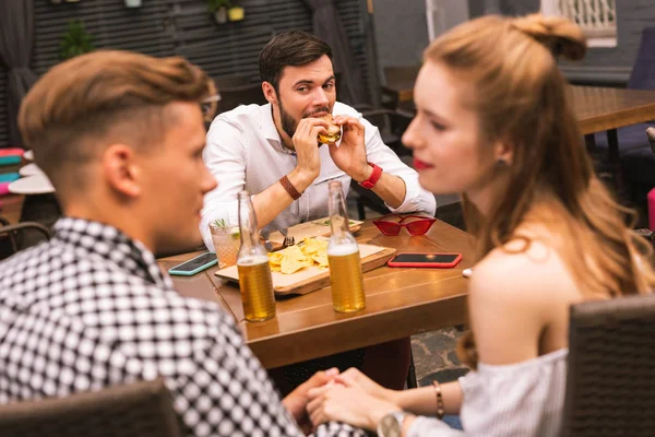 Dva lidé drží ruce a jejich přítel jíst hamburgery — Stock fotografie