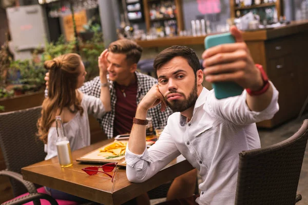 Hombre molesto tomando selfies mientras sus amigos coquetean —  Fotos de Stock