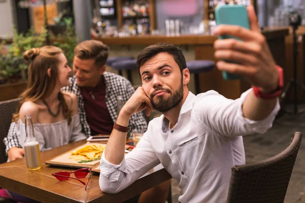 Jovem tomando selfies enquanto se sente entediado com amigos — Fotografia de Stock