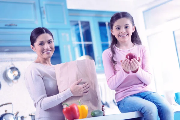 Happy girl holding red apple and her mother standing near — Stock Photo, Image