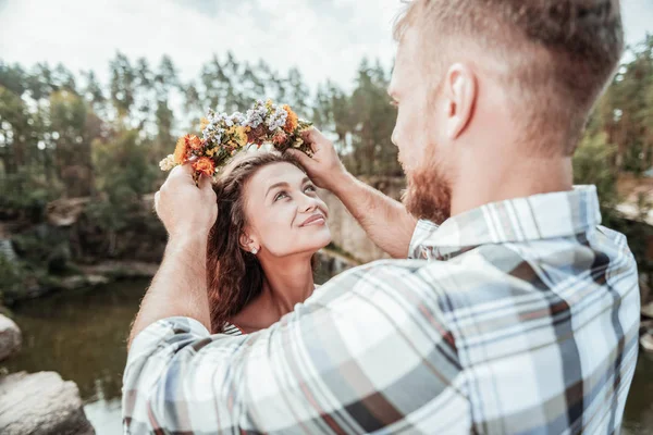 Vårdande skäggiga blonda mannen att sätta fina blommiga halsband på hans flickvän — Stockfoto