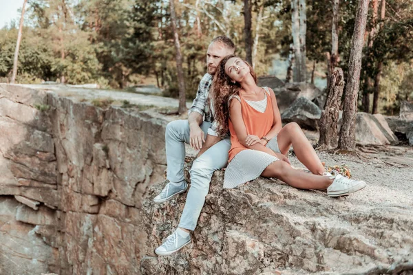 Schöne dunkelhaarige Frau stützt sich auf ihren starken Mann, während sie in der Nähe von Klippen sitzt — Stockfoto