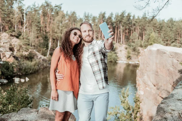 Χαμογελώντας blonde-haired άνθρωπος λήψης selfie με την ελκυστική κοπέλα κοντά στη λίμνη — Φωτογραφία Αρχείου