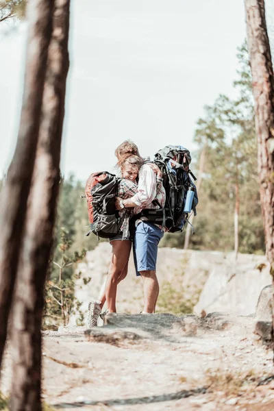 Tender woman with heavy backpack hugging her strong bearded man while hiking