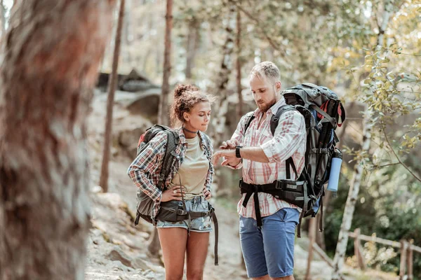 Skäggiga backpacker kontroll tid på sin svart klocka medan vandring med flickvän — Stockfoto